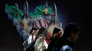 Des femmes iraniennes passent devant une banderole montrant des missiles lancés depuis une carte iranienne à Téhéran, le 19 avril 2024.